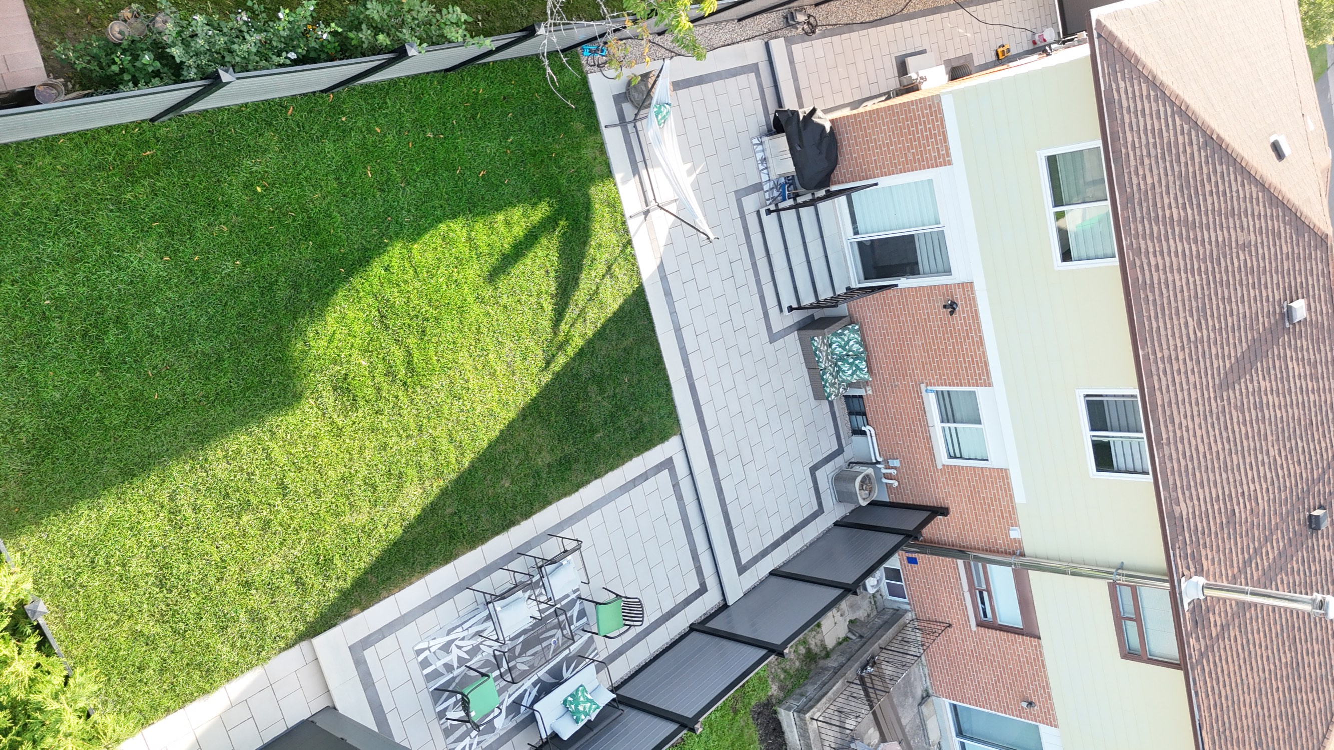 Aerial after photo of the same Mississauga backyard with a bordered interlocking paver patio, separate seating pad, new steps and fresh sod