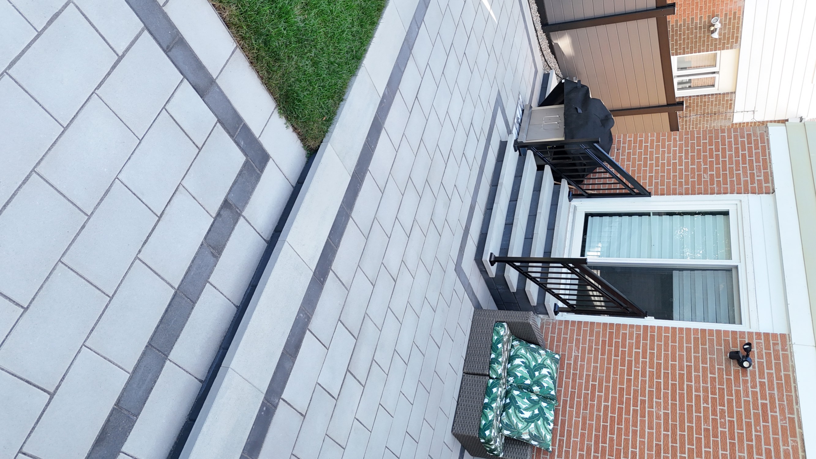 Close-up of the finished interlocking patio in Mississauga showing light grey pavers with a charcoal soldier-course border, new stone entry steps with black railing, and a built-in BBQ corner