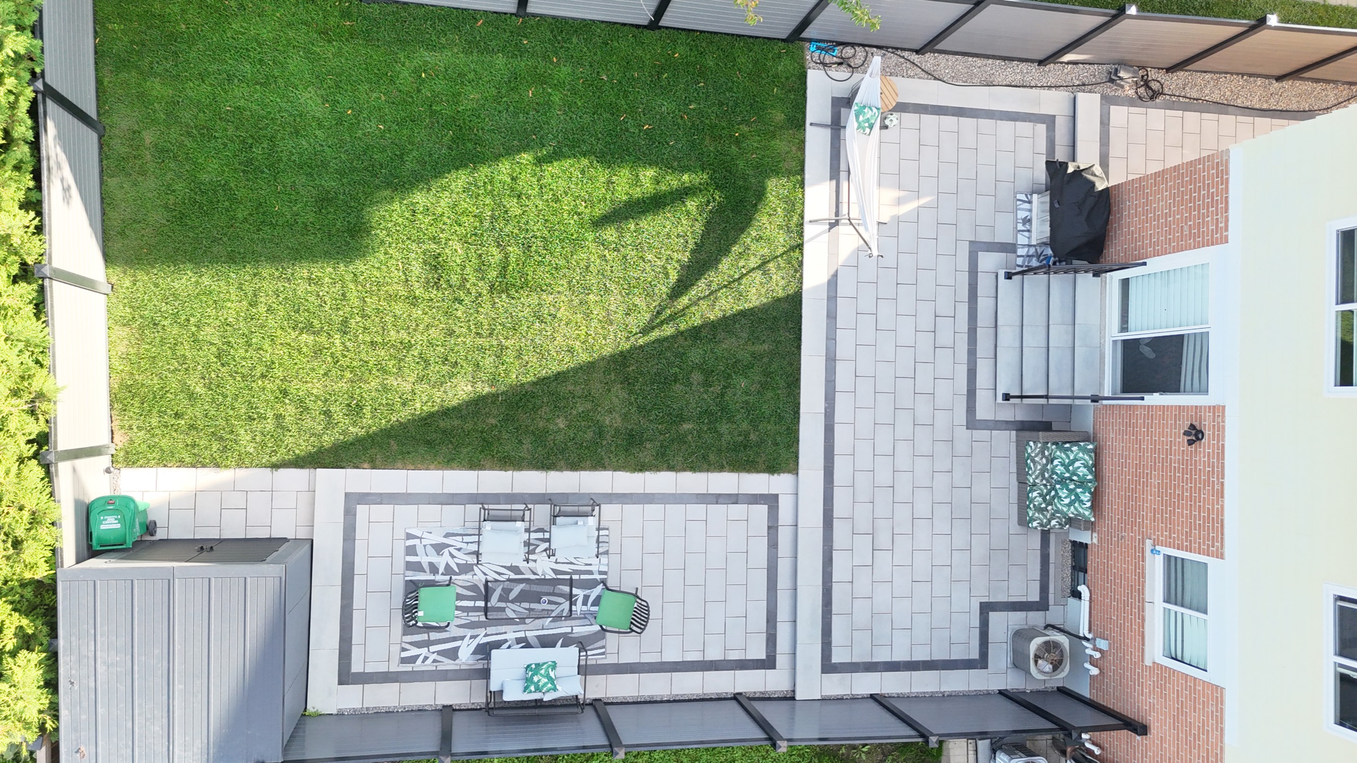 Top-down drone photo of the finished Mississauga backyard showing the full-width interlocking patio, connecting walkway, bordered seating pad with outdoor furniture, and new sod lawn